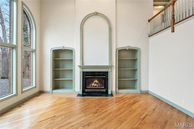 unfurnished living room with a towering ceiling, wood finished floors, a premium fireplace, and baseboards