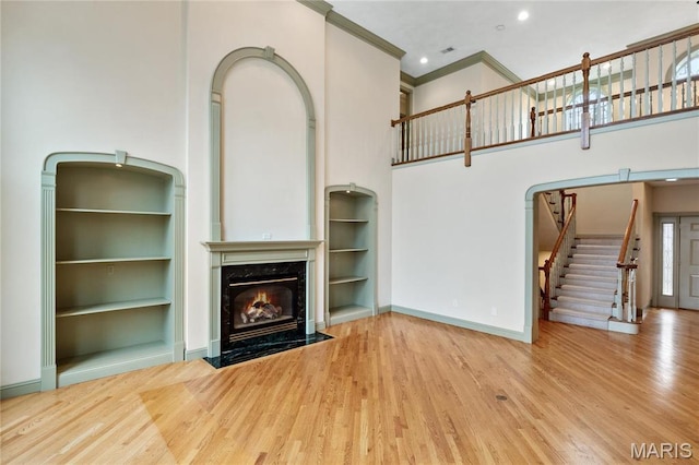 unfurnished living room with a premium fireplace, wood finished floors, crown molding, stairs, and a high ceiling
