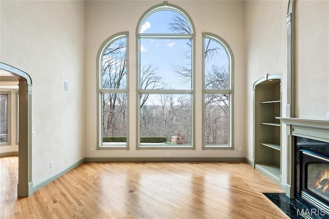 unfurnished living room with wood finished floors, baseboards, and built in shelves
