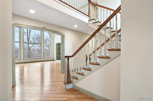 stairway featuring wood finished floors, a towering ceiling, and recessed lighting