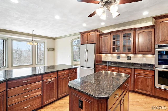 kitchen with stainless steel appliances, light wood-style floors, a center island, a ceiling fan, and glass insert cabinets