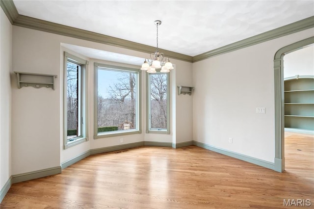 unfurnished dining area featuring a chandelier, wood finished floors, crown molding, baseboards, and arched walkways