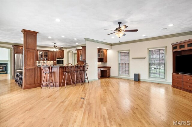 living room featuring a ceiling fan, recessed lighting, ornamental molding, light wood-style flooring, and a glass covered fireplace