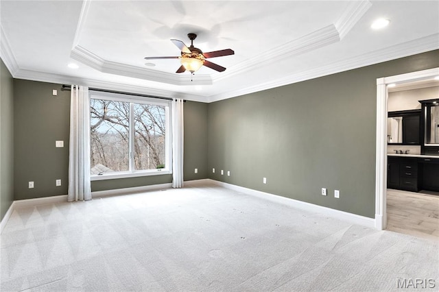 empty room with ceiling fan, ornamental molding, light colored carpet, a raised ceiling, and baseboards