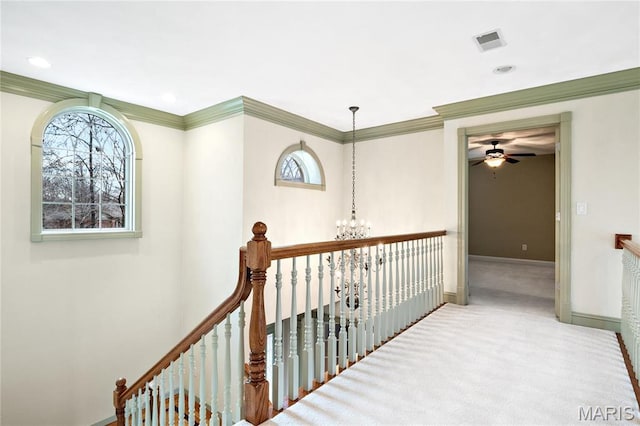 hall with an upstairs landing, a chandelier, baseboards, carpet floors, and ornamental molding