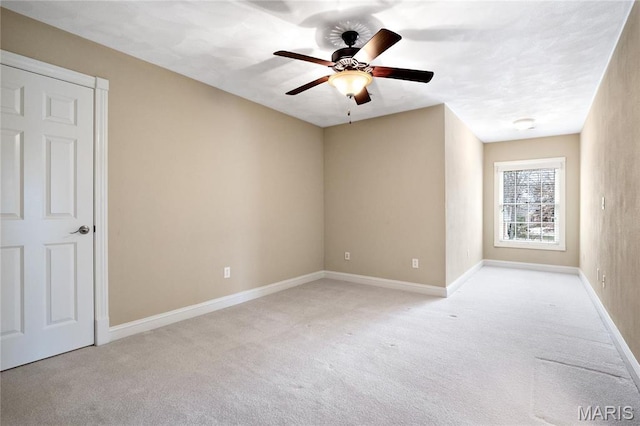 spare room featuring light carpet, ceiling fan, and baseboards