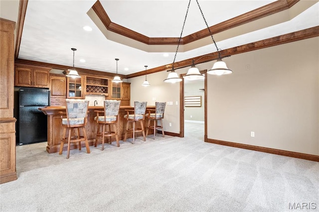 kitchen featuring freestanding refrigerator, ornamental molding, brown cabinetry, a breakfast bar, and light colored carpet