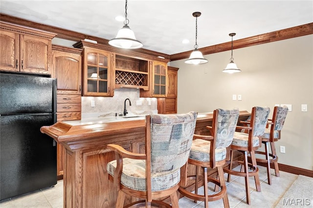 indoor wet bar featuring freestanding refrigerator, crown molding, decorative backsplash, pendant lighting, and baseboards