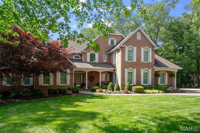 view of front of home featuring a front yard, a porch, brick siding, and roof with shingles