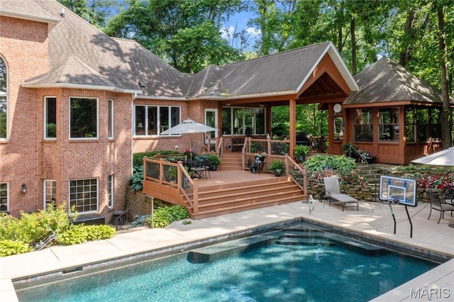 rear view of property featuring a deck, an outdoor pool, brick siding, and a patio area