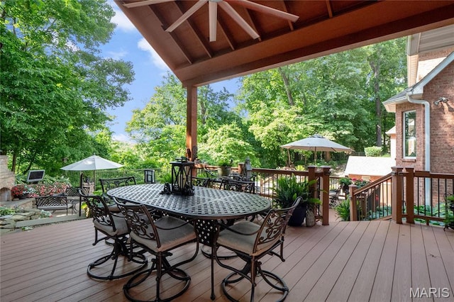 wooden terrace featuring outdoor dining space and view of wooded area