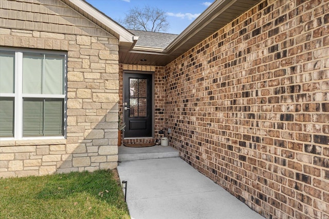 view of exterior entry with brick siding, stone siding, and roof with shingles