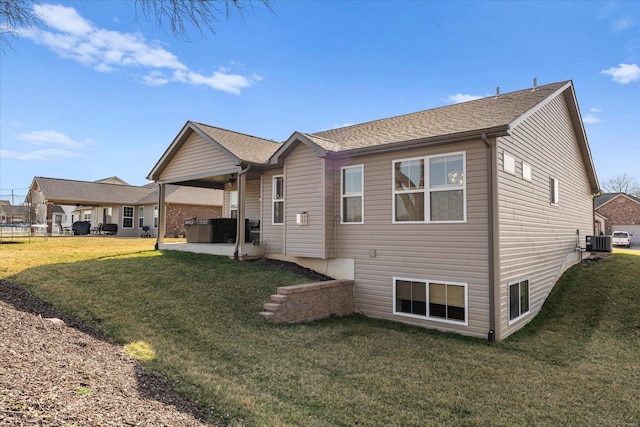 back of property featuring central air condition unit, a hot tub, a ceiling fan, and a lawn