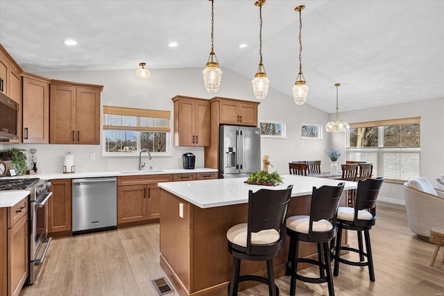 kitchen with appliances with stainless steel finishes, a sink, lofted ceiling, brown cabinets, and recessed lighting