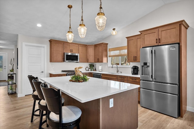 kitchen with appliances with stainless steel finishes, a sink, lofted ceiling, a center island, and brown cabinetry