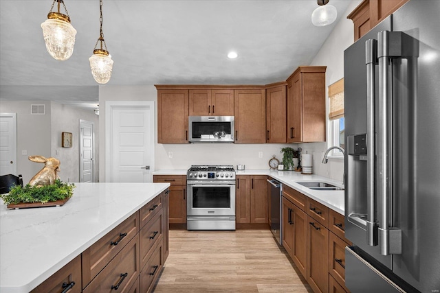kitchen featuring appliances with stainless steel finishes, a sink, light wood-style floors, hanging light fixtures, and brown cabinets