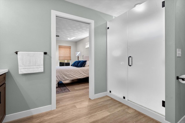 ensuite bathroom featuring baseboards, wood finished floors, vanity, and a stall shower