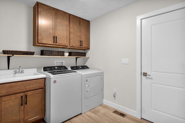 clothes washing area with washing machine and clothes dryer, light wood-type flooring, baseboards, and cabinet space
