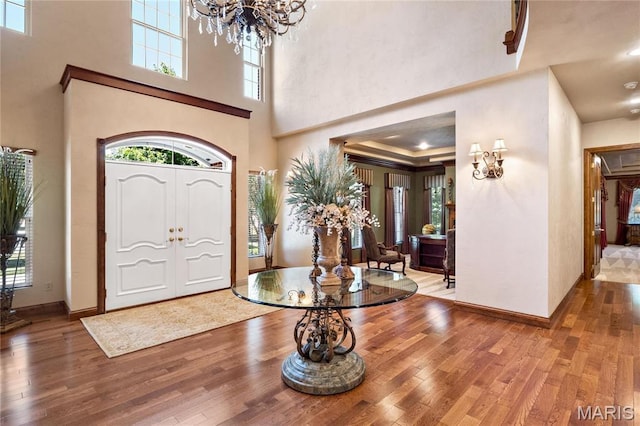 entrance foyer with a towering ceiling, a chandelier, wood finished floors, and baseboards