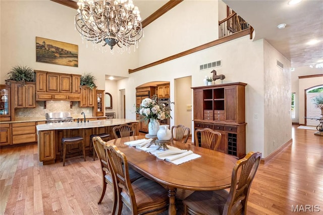 dining space featuring light wood-style floors, a chandelier, arched walkways, and a high ceiling