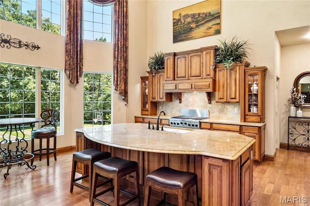 kitchen featuring a towering ceiling, brown cabinetry, a sink, light wood-style flooring, and baseboards