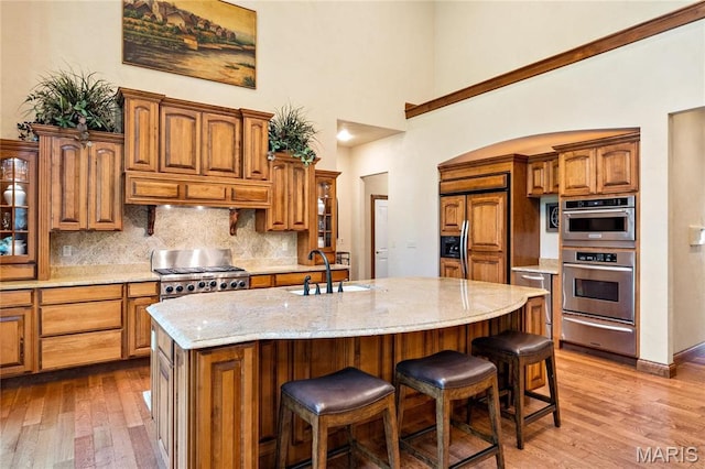 kitchen featuring a warming drawer, wood finished floors, tasteful backsplash, glass insert cabinets, and a high ceiling