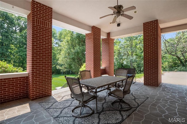 view of patio featuring ceiling fan, outdoor dining space, and view of scattered trees