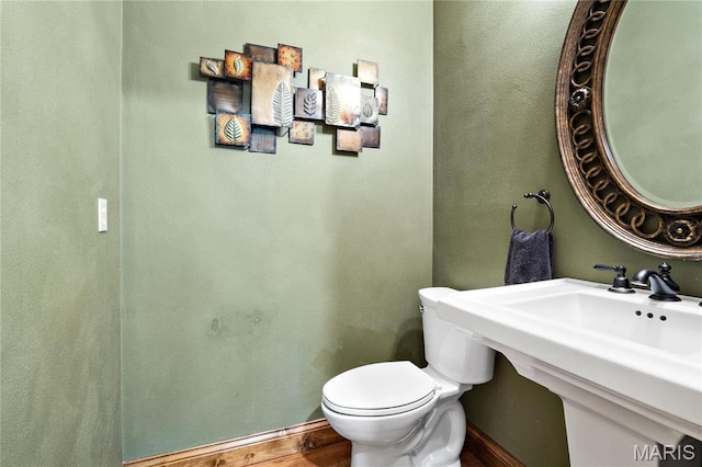 half bath with toilet, baseboards, and a sink