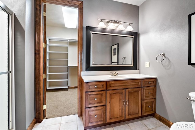 bathroom featuring toilet, tile patterned flooring, vanity, baseboards, and a spacious closet