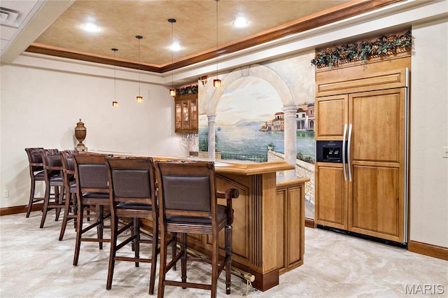 indoor bar with paneled built in fridge, a raised ceiling, baseboards, ornamental molding, and hanging light fixtures