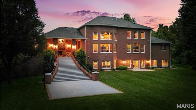 back of house at dusk featuring a patio area, a lawn, and stairway
