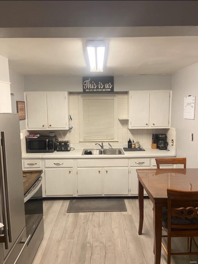 208 John R, Kennett, MO 63857 - kitchen featuring stainless steel appliances, a sink, light countertops, white cabinetry, and decorative backsplash