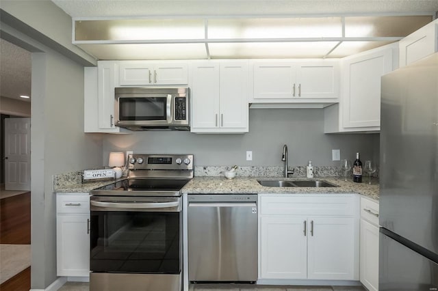 kitchen featuring stainless steel appliances, a sink, white cabinets, and light stone countertops