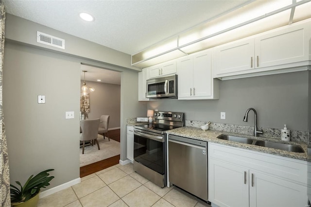 kitchen featuring appliances with stainless steel finishes, a sink, white cabinets, light stone counters, and light tile patterned floors