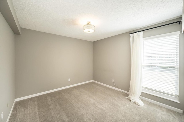 unfurnished room with light colored carpet, baseboards, and a textured ceiling