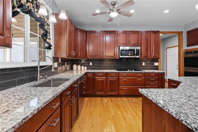 kitchen with a sink, stainless steel appliances, light wood-style flooring, a ceiling fan, and light stone countertops