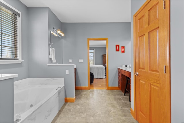 bathroom with ensuite bathroom, a tub with jets, baseboards, and vanity