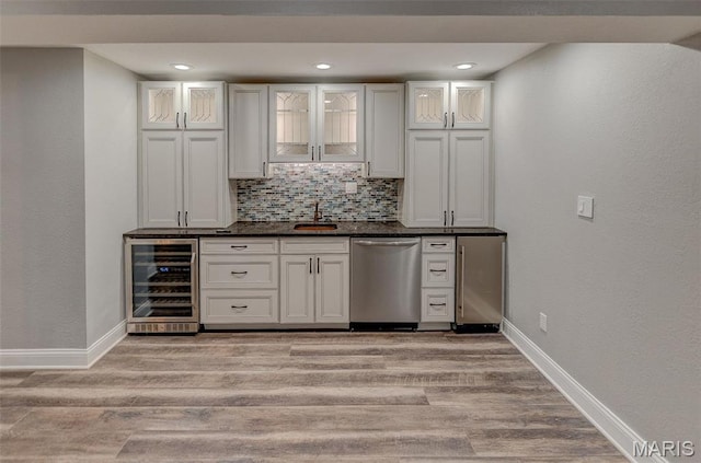 indoor wet bar featuring dishwasher, wine cooler, baseboards, light wood-style flooring, and backsplash