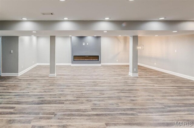 finished below grade area featuring baseboards, wood finished floors, recessed lighting, and a glass covered fireplace