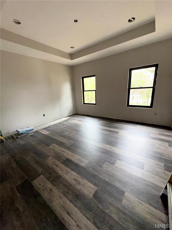 empty room featuring a tray ceiling, wood finished floors, baseboards, and recessed lighting