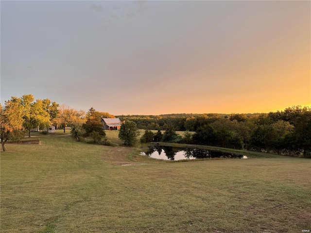 yard at dusk featuring a water view and a yard