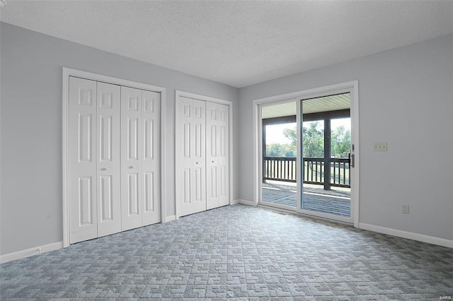 unfurnished bedroom with access to outside, two closets, carpet floors, a textured ceiling, and baseboards