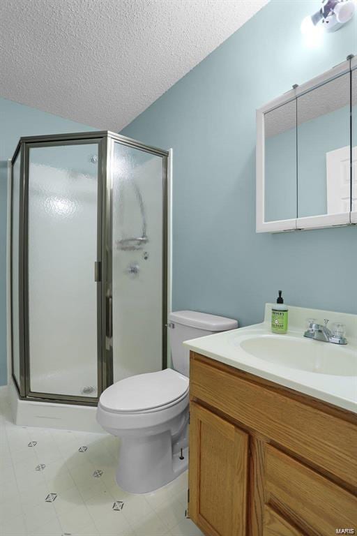 bathroom featuring a shower stall, vanity, toilet, a textured ceiling, and tile patterned flooring