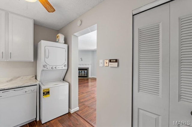 1436 Peacock Ln, Saint Louis, MO 63144 - laundry room with stacked washer / drying machine, dark wood-style flooring, a ceiling fan, a textured ceiling, and a glass covered fireplace