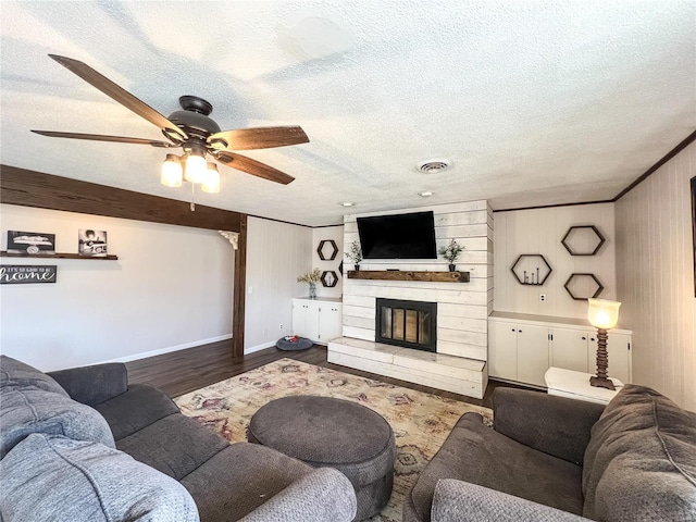 living room featuring ceiling fan, a textured ceiling, wood finished floors, a fireplace, and baseboards