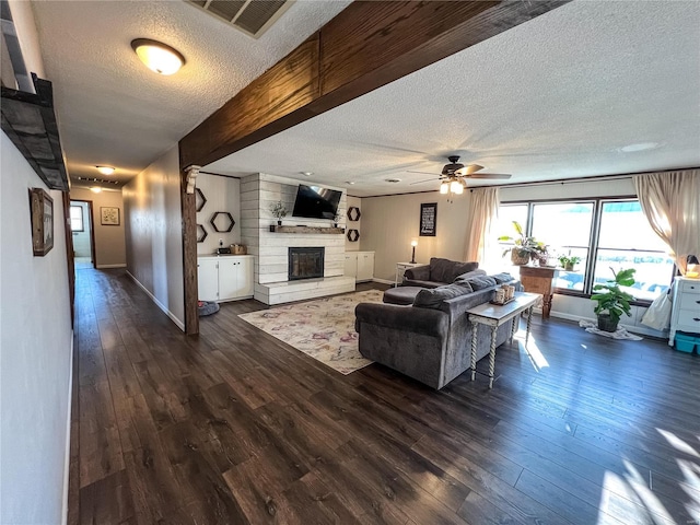 living area with a textured ceiling, dark wood-type flooring, a brick fireplace, ceiling fan, and baseboards