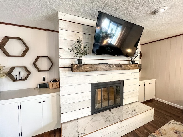 detailed view of a textured ceiling, wood finished floors, baseboards, a glass covered fireplace, and crown molding