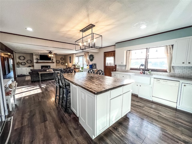 kitchen with white dishwasher, wooden counters, a textured ceiling, a sink, and open floor plan