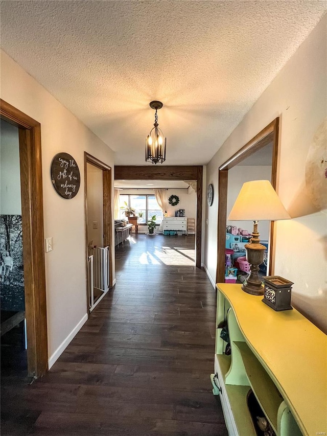 corridor featuring dark wood-style floors, a chandelier, a textured ceiling, and baseboards