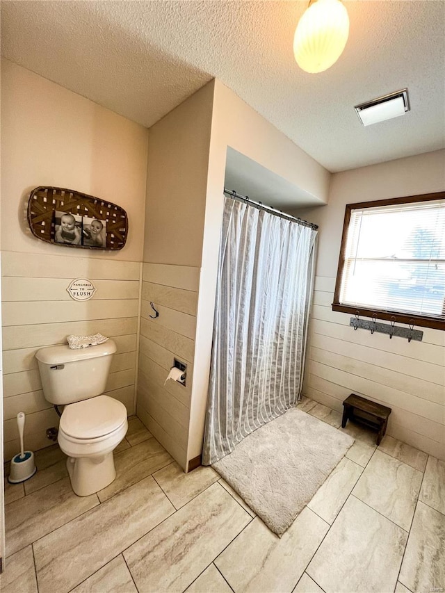 full bath with curtained shower, a textured ceiling, toilet, and wainscoting